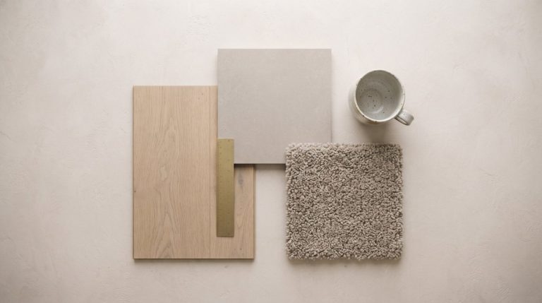 Overhead arrangement of oak plank, stone-look tile and carpet flooring samples on a pale plaster surface